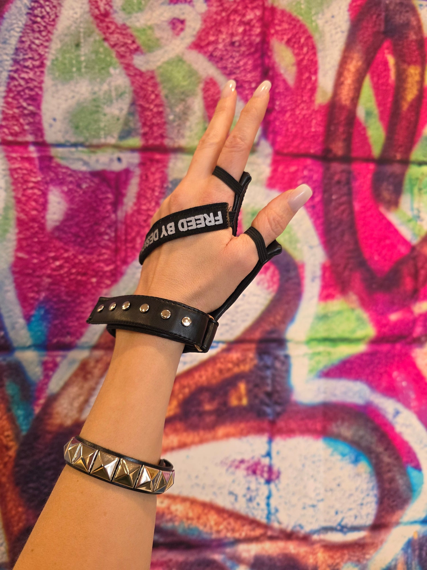 Hand wearing a black disability glove featuring reflective Freed By Design across the hand, against a colorful graffiti background