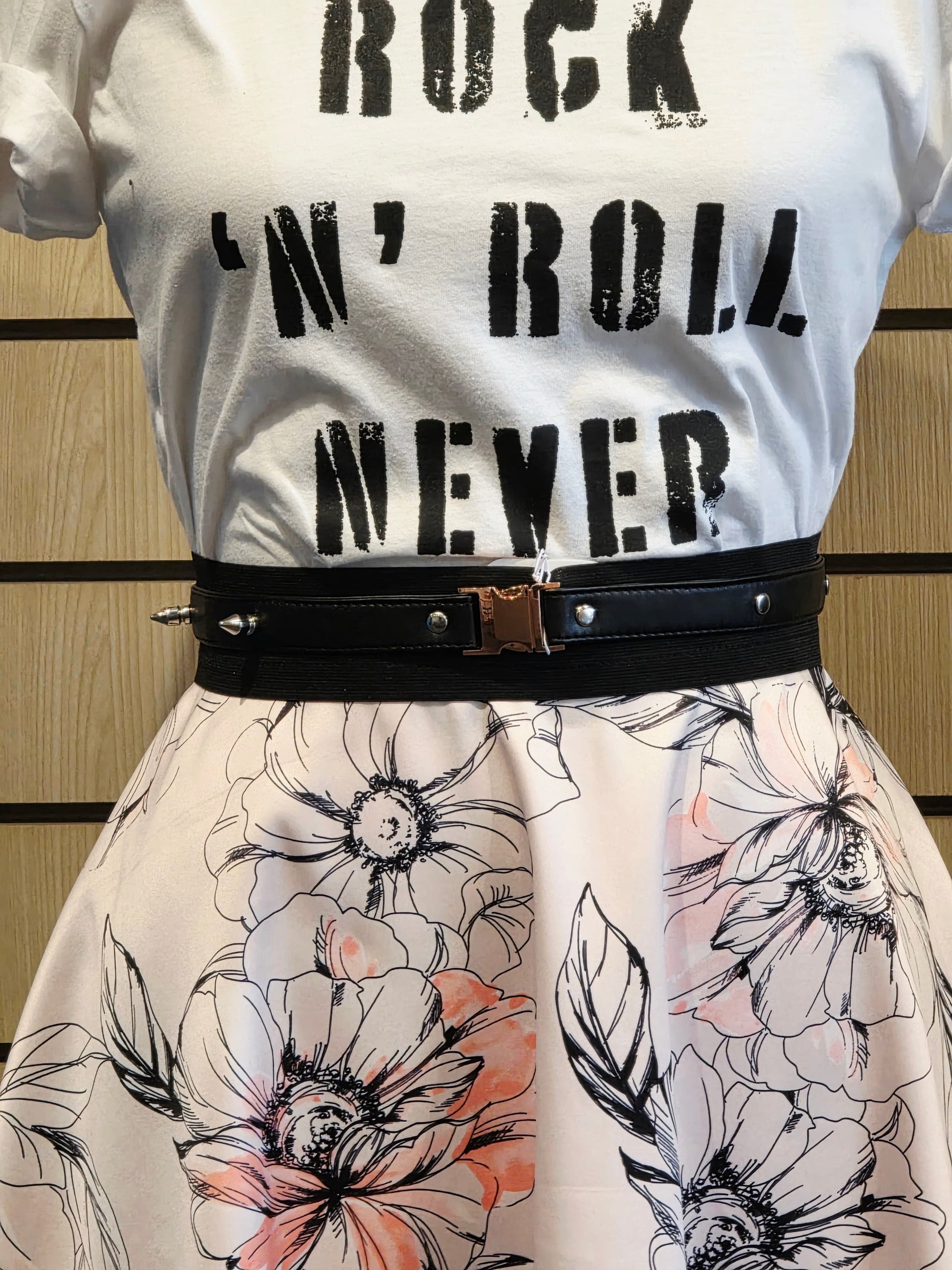 White t-shirt with 'Rock 'n' Roll Never' text and floral skirt and black studded faux leather belt on a striped background