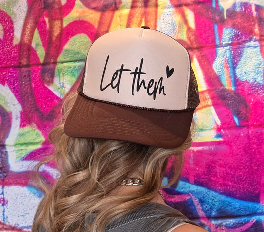 Person wearing a cap with 'Let them' text against a colorful graffiti wall