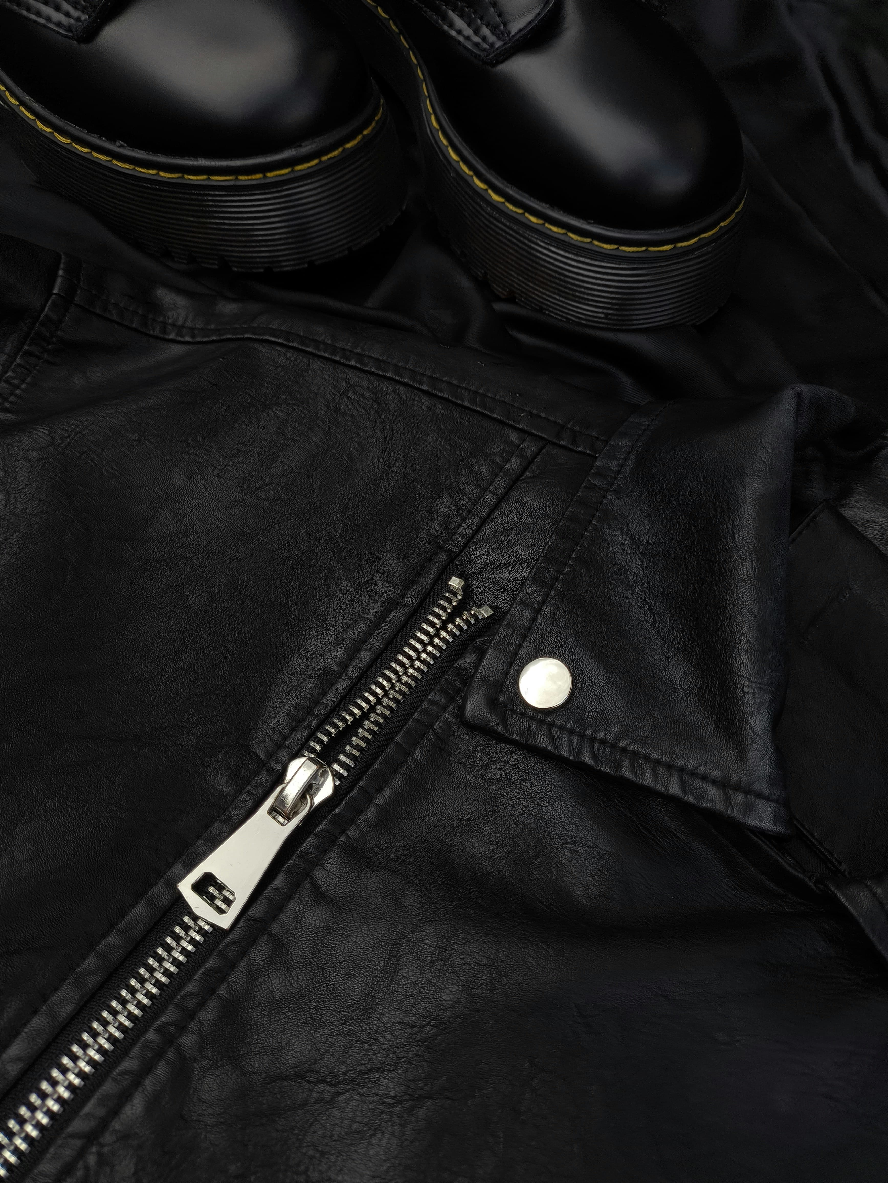 Close-up of a black leather jacket with a zipper and shoes in the background