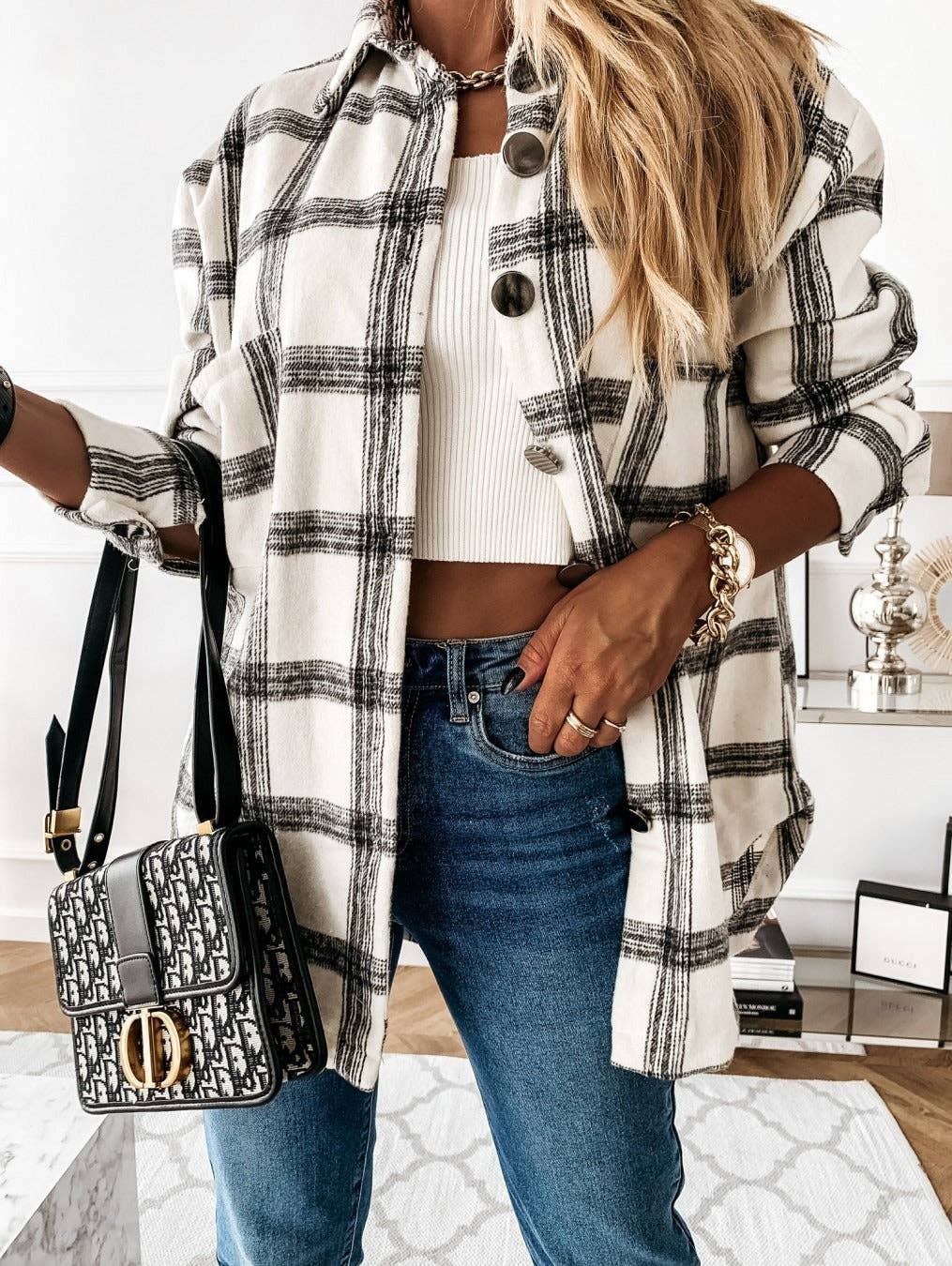 Person wearing a plaid shirt over a white top and blue jeans, holding a black and gold handbag.