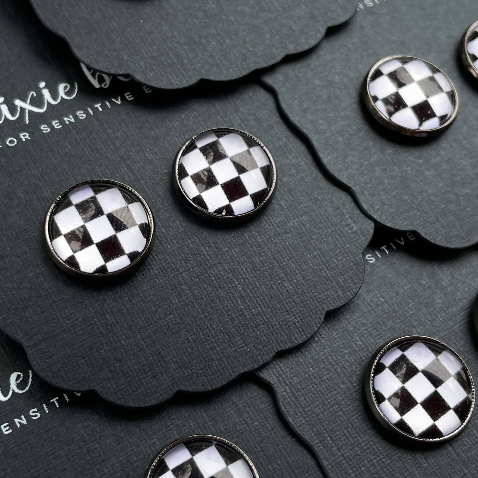 Black and white checkered earrings on a black card with 'Pixie' branding.
